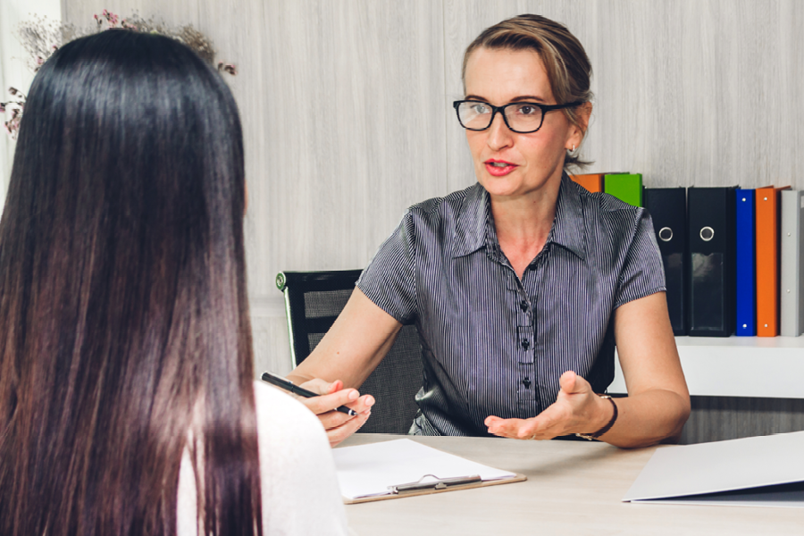 A college professor holding a pencil is meeting with a college student at a desk for counseling.